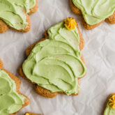 A sugar cookie shaped like a Christmas tree with green icing and a yellow icing star on top surrounded by other sugar cookies.