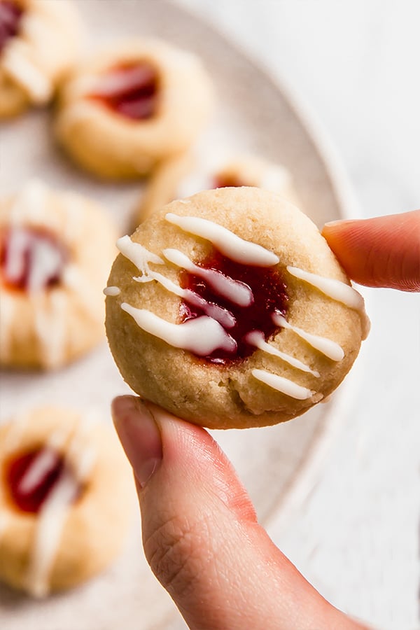 thumbprint cookies on plate, one cookie held up close with fingers