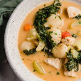 Tuscan chicken soup in a bowl with an orange broth, kale, chicken and veggies.