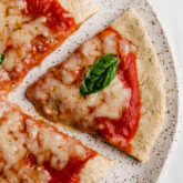 Tigernut flour pizza slice on a plate topped with a piece of basil.