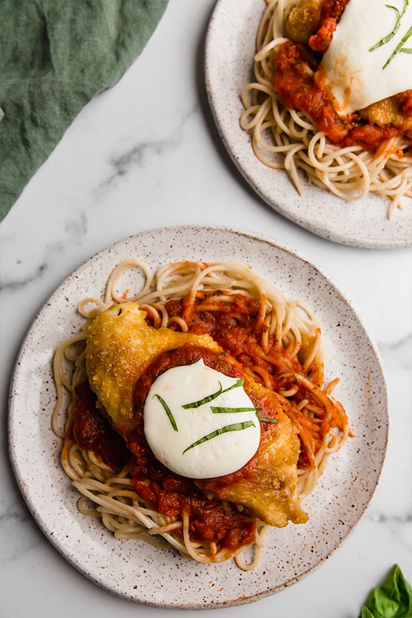 Two plates of chicken parmesan with spaghetti