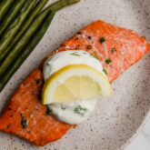 Baked salmon topped with creamy lemon dill sauce and a lemon slice.