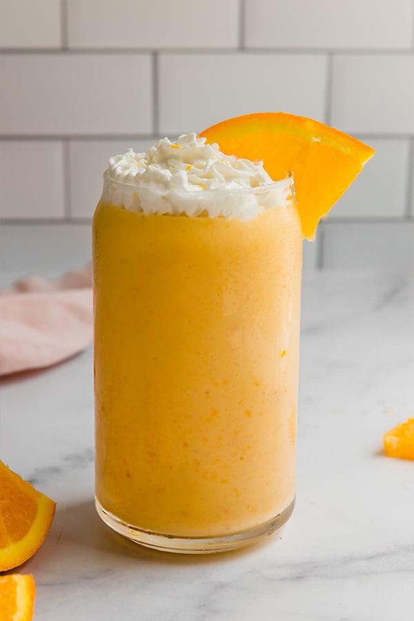 Orange creamsicle smoothie in a glass with whipped cream and an orange slice on top