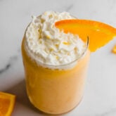 Whipped coconut cream and an orange slice on an orange creamsicle smoothie.