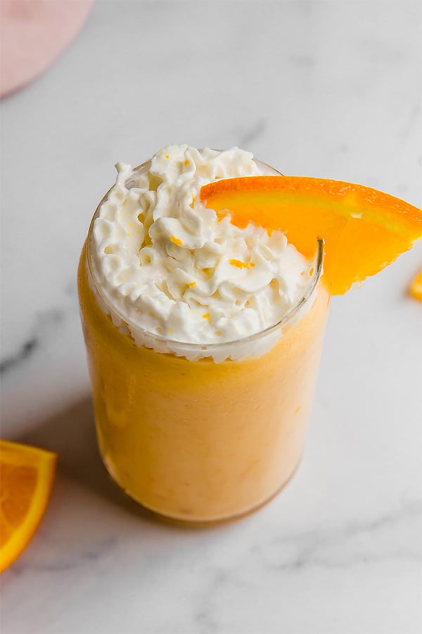Top view of orange creamsicle smoothie in a glass with whipped cream and an orange slice on top