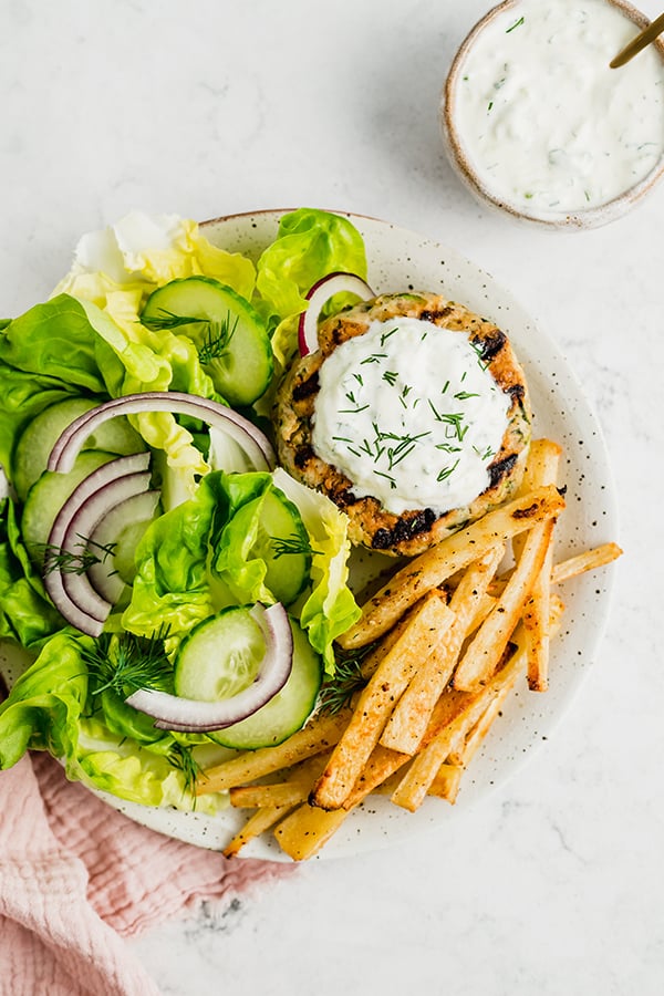 Grilled greek chicken burger with toppings and fries on a plate