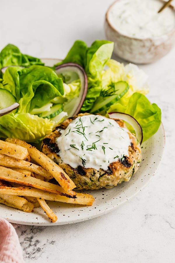 Grilled greek chicken burger on a plate with greens and fries