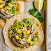 Several mango chicken tostadas on a lined baking sheet.