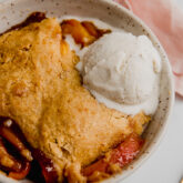 Ice cream over peach cobbler in a bowl.