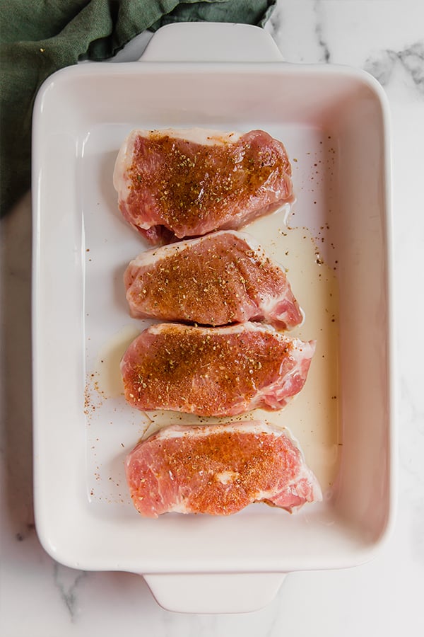 4 boneless pork chops seasoned and ready to bake in a baking dish
