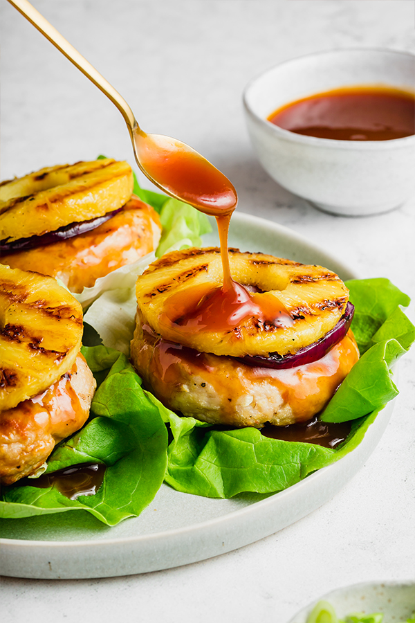 Chicken burgers on plate with spoon drizzling sauce over top