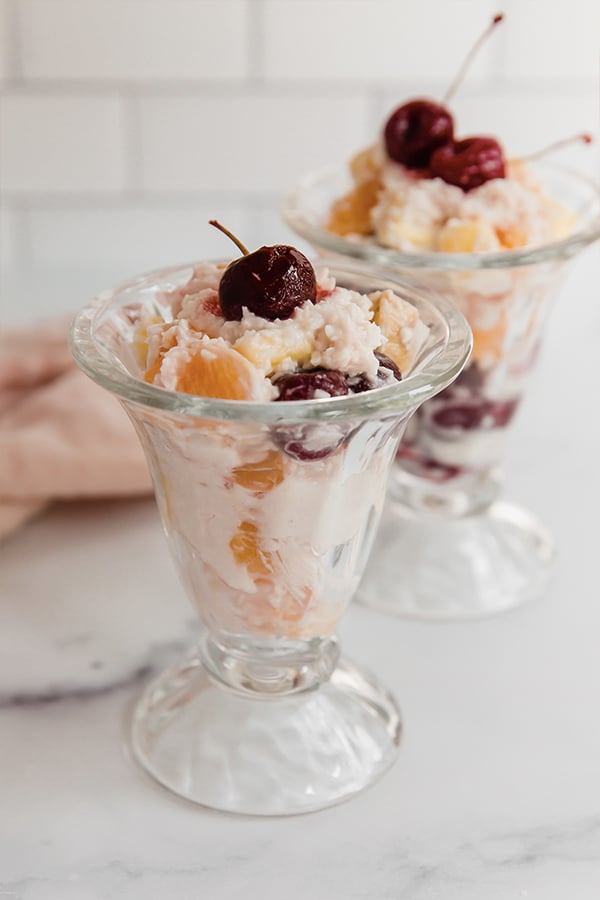 Ambrosia salad served in glass jars with cherries on top