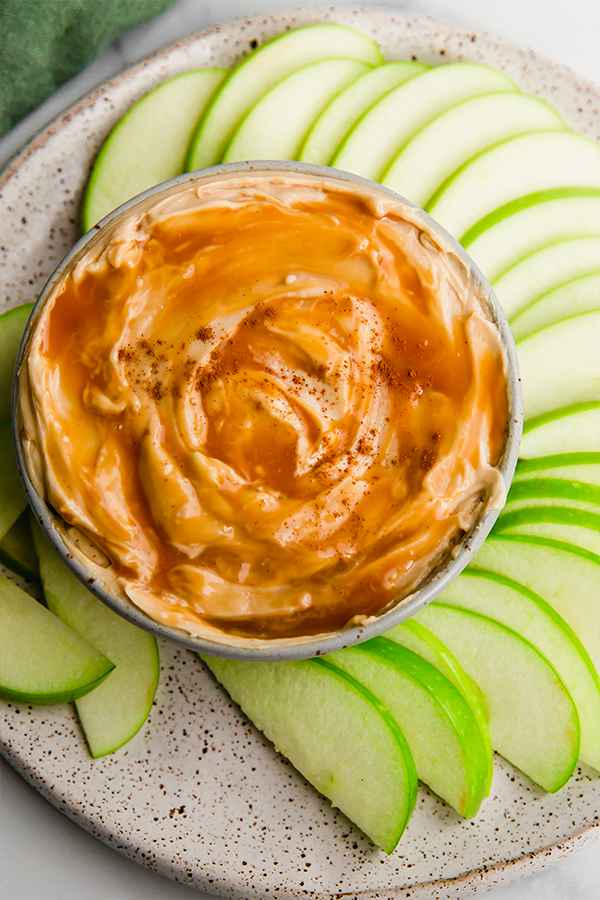 Creamy caramel apple dip surrounded by apple slices on a plate.