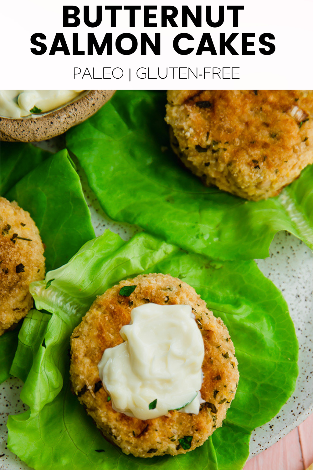 A high-angle view of several golden-brown butternut salmon cakes, garnished with fresh parsley, presented on a white plate with a green background.