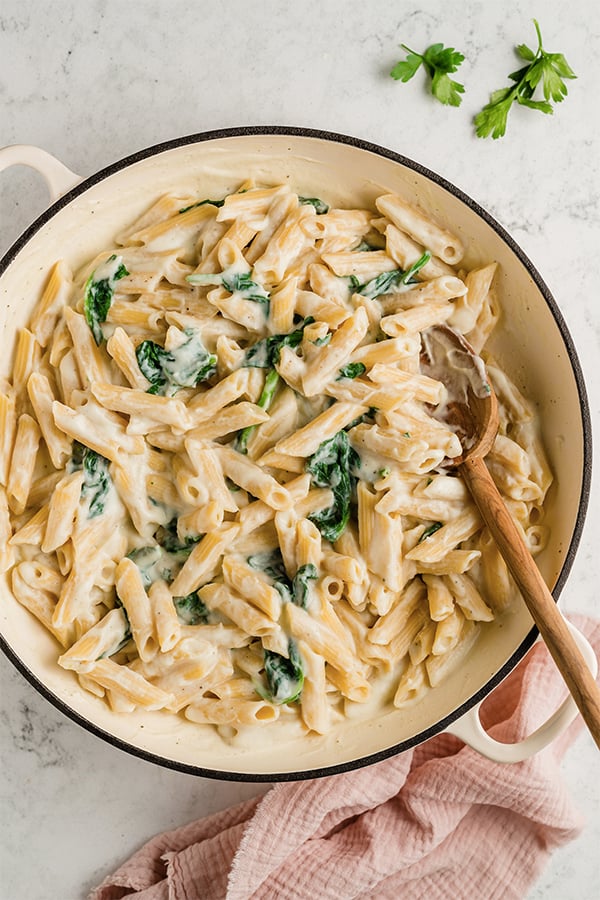 A pot of Easy Penne Alfredo with a wooden spoon in it.