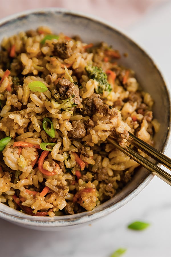 Chopsticks dipping into a bowl of ground beef fried rice.