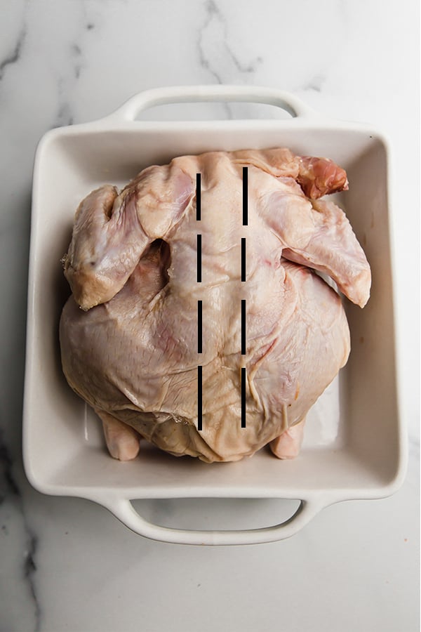 A raw chicken in a white baking dish.