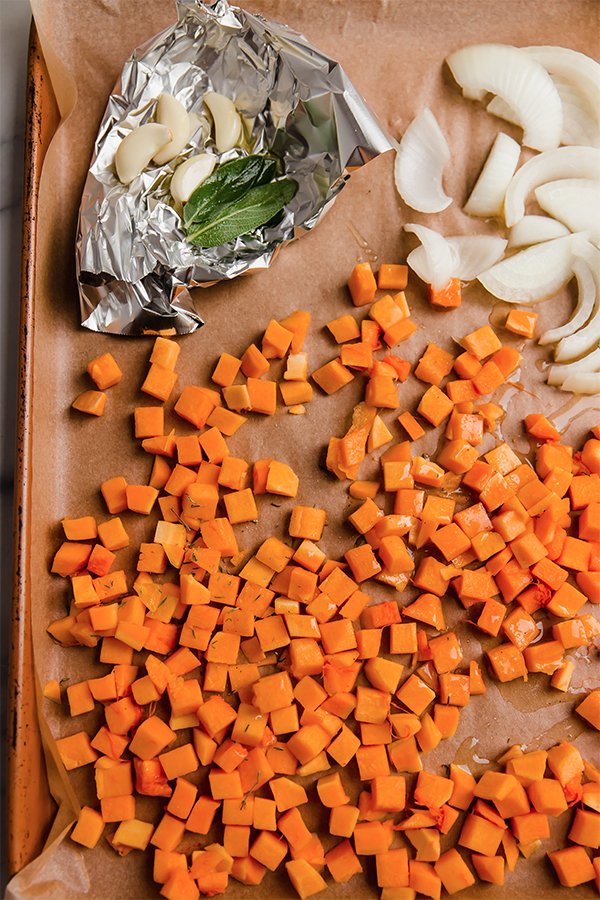 A sheet pan with sliced onion, garlic, and butternut squash.