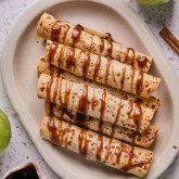 Apple pie roll ups on a platter drizzled with caramel.