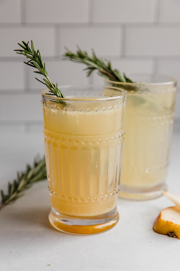 Two ginger pear mocktails in glasses with rosemary garnish on a white background