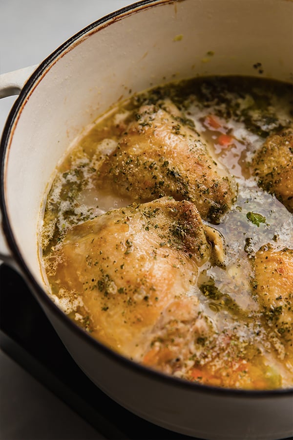 Seasoned chicken in broth in a pot.