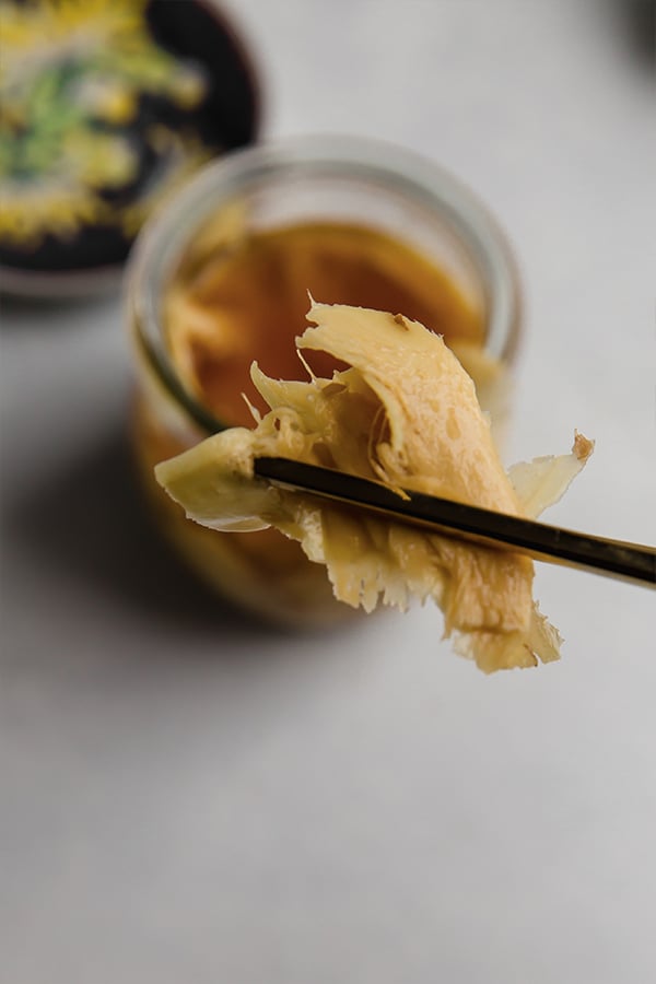 Chopsticks lifting pickled ginger out of a jar.