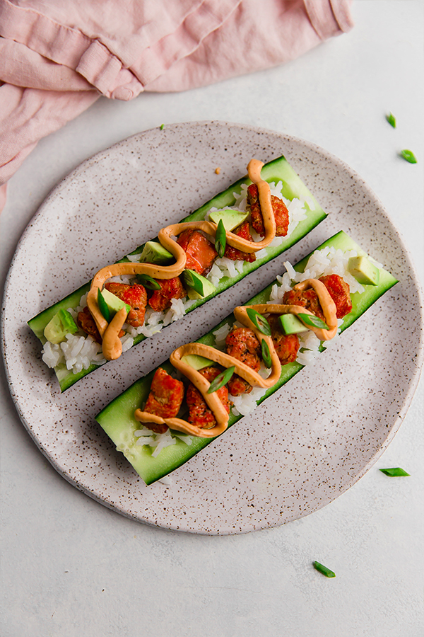 A plate with two salmon cucumber sushi boats on it.