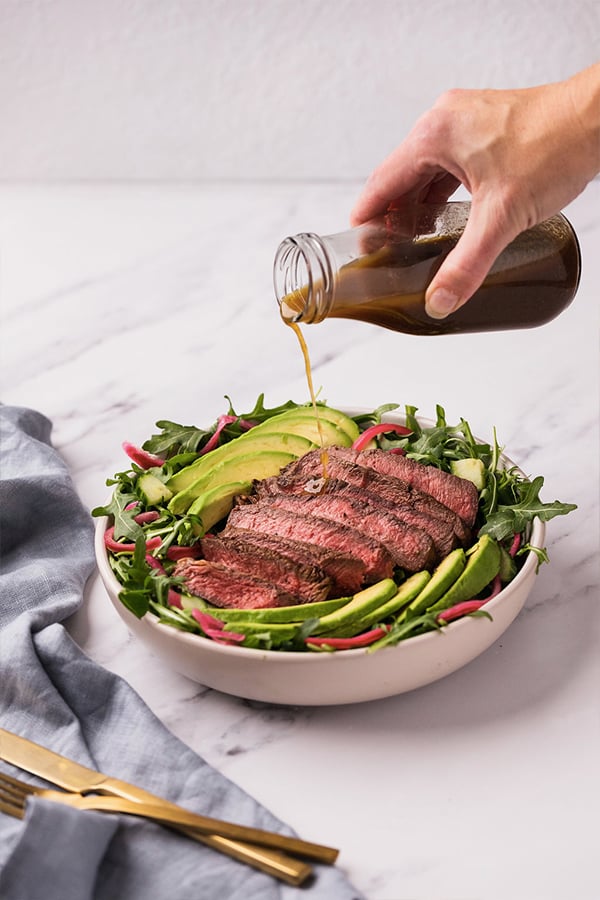 Pouring dressing onto the balsamic steak salad.