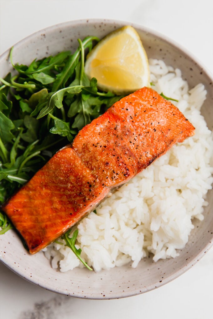 A bowl with air fryer salmon, arugula, and steamed rice.