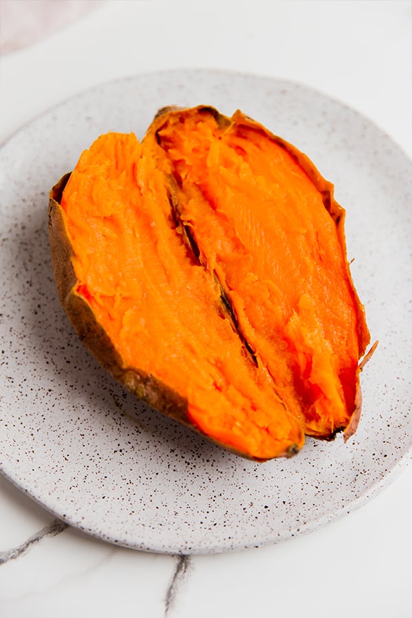 A sweet potato cut in half and open on a plate.