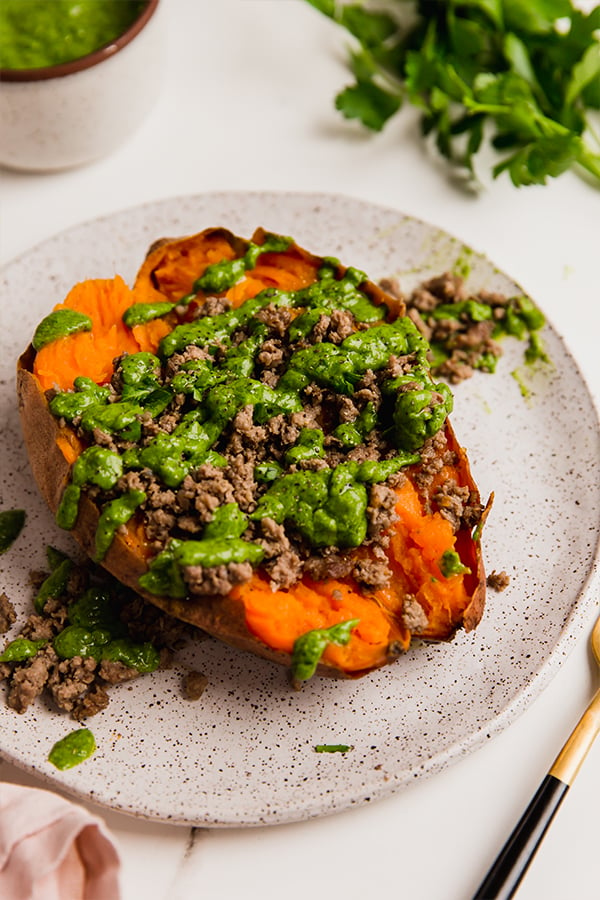 A ground beef stuffed sweet potato with avocado chimichurri on a plate.
