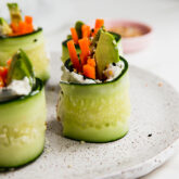 Smoked salmon bagel cucumber rolls standing up on a plate.