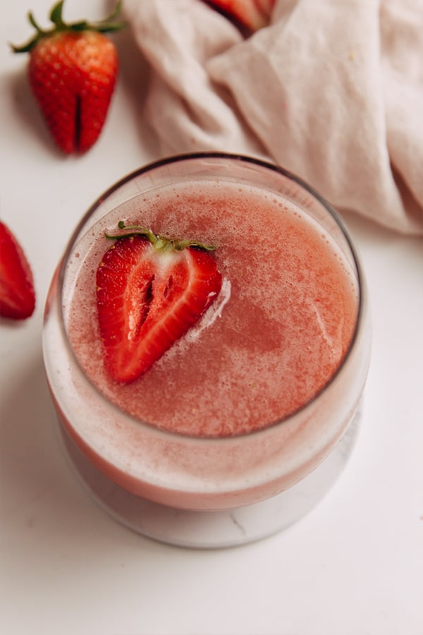A glass of frose with strawberry in it.