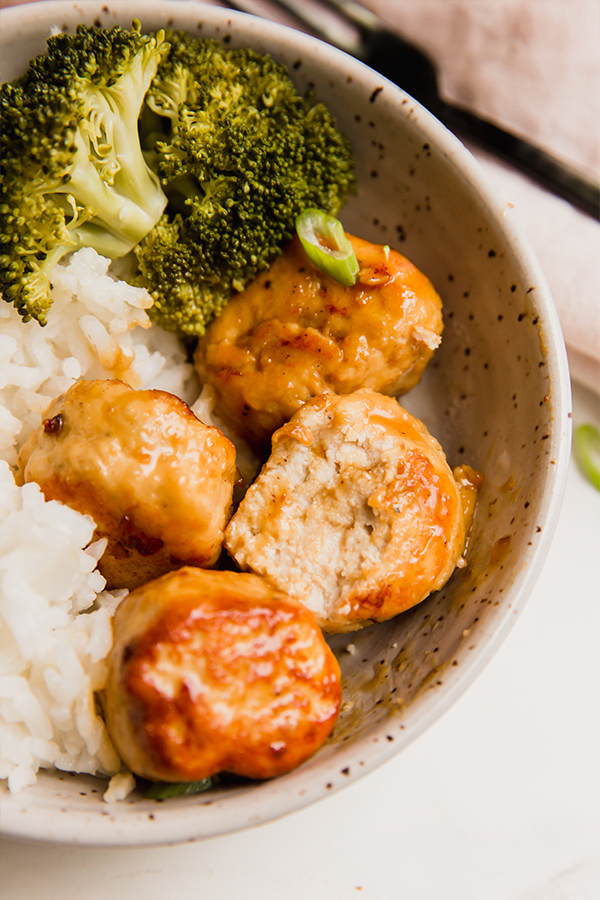 A bowl with rice, orange chicken meatballs, and broccoli.