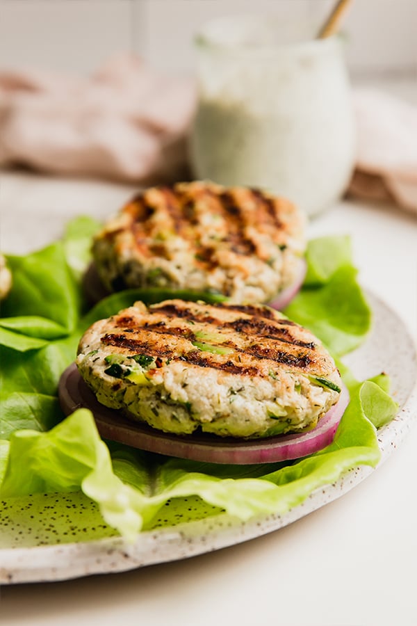 Avocado ranch chicken burgers on lettuce on a plate.