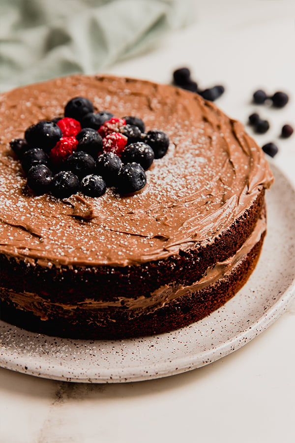 A shot of the full paleo chocolate cake with frosting and berries.