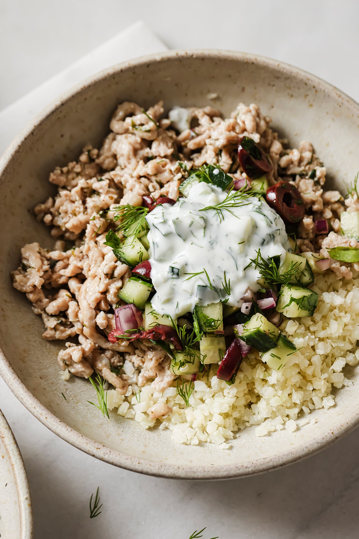 Greek ground chicken bowl topped with tzatiki and dill.
