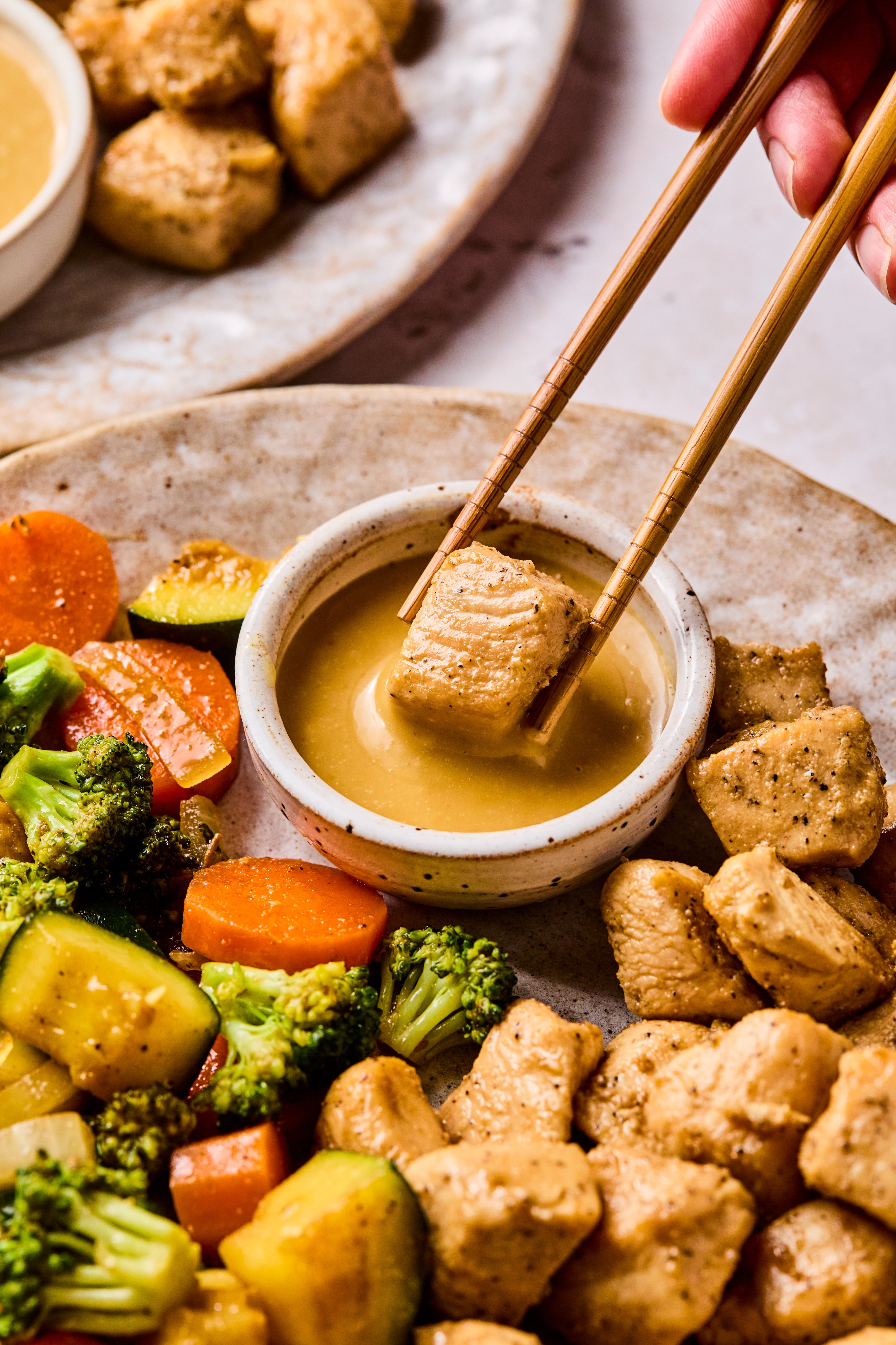 Hibachi chicken being dipped in mustard sauce with chopsticks.