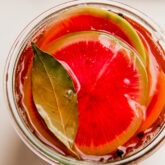 Thin slices of watermelon radish in liquid topped with a bay leaf.