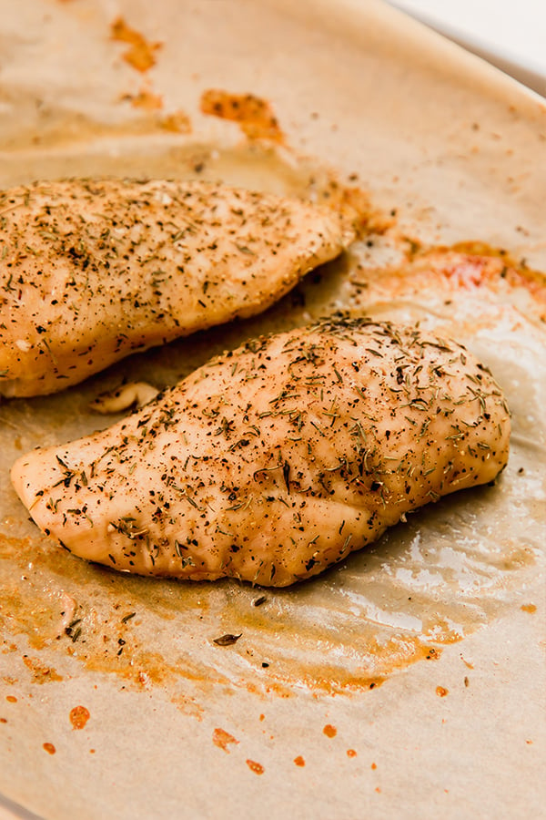 Chicken breasts seasoned on baking sheet.