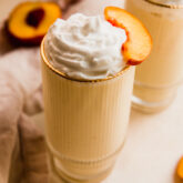 Dairy-free creamy peach milkshake in a tall glass with a peach slice.