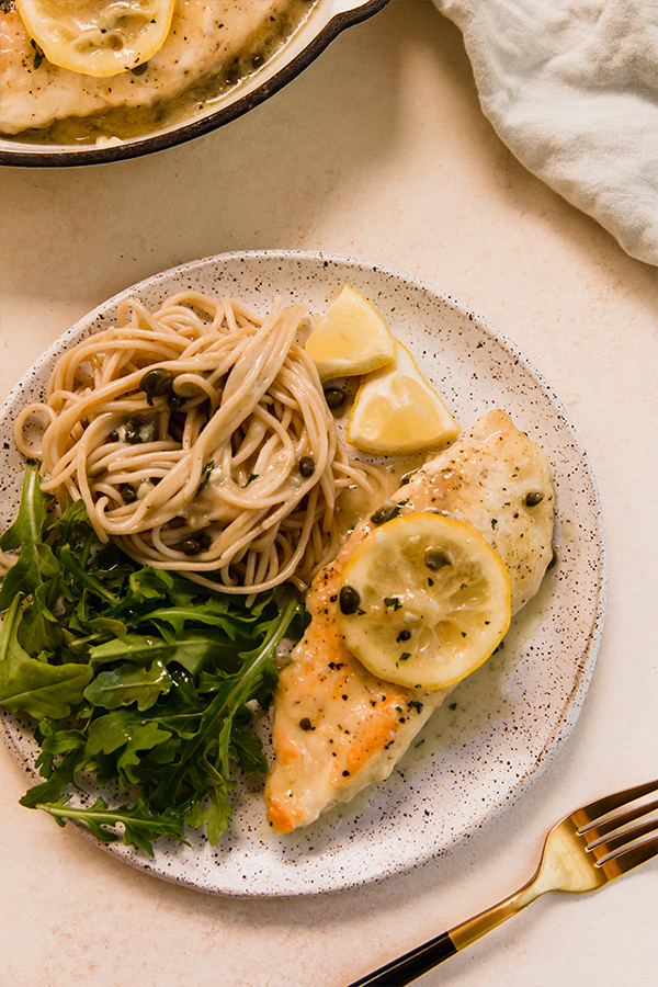 Chicken piccata plated with kale and pasta.
