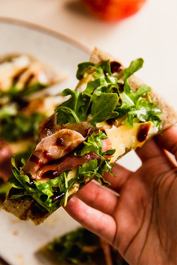 A slice of apple balsamic flatbread in a hand.