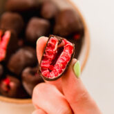 Person holding a layered chocolate covered frozen raspberry cut in half.