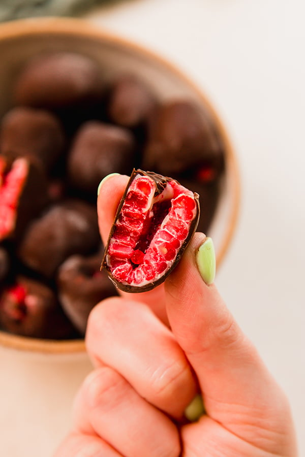 A chocolate frozen raspberry being held between fingers.