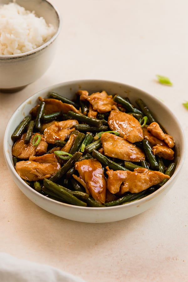 string beans chicken in a bowl with a bowl on rice in the background