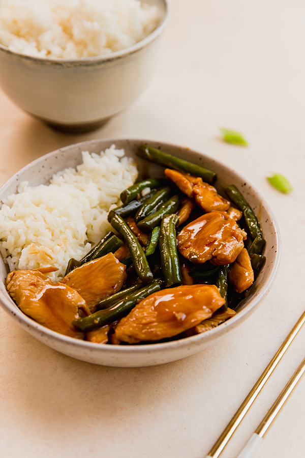 string beans chicken in a bowl with rice with another bowl of rice in the background