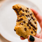 Person holding a large pumpkin chocolate chip cookie missing a bite.