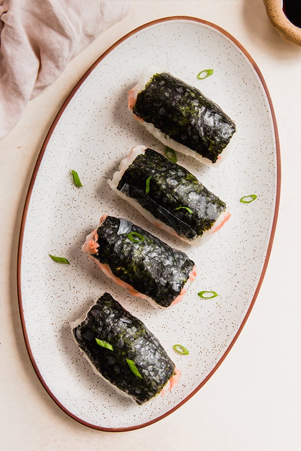 A plate with sushi inspired salmon rice paper rolls on it.