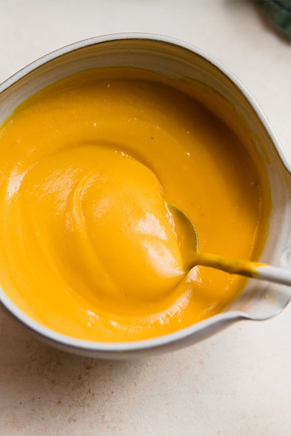 A bowl of dairy-free cheese sauce with a spoon.